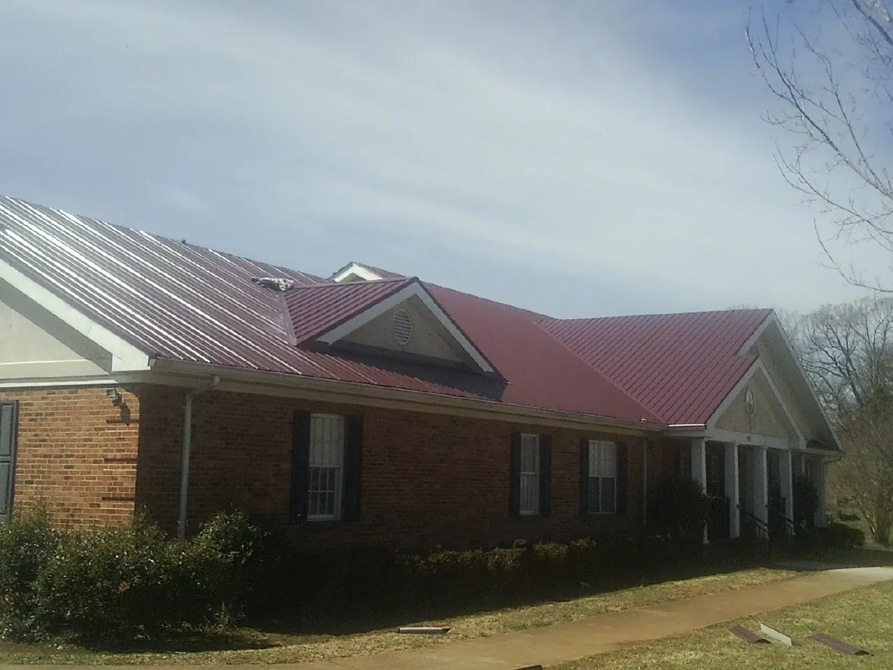 Red metal roof with gabled entries on a long brick building, from a Hail Damage Roof Repair job in Dammeron Valley