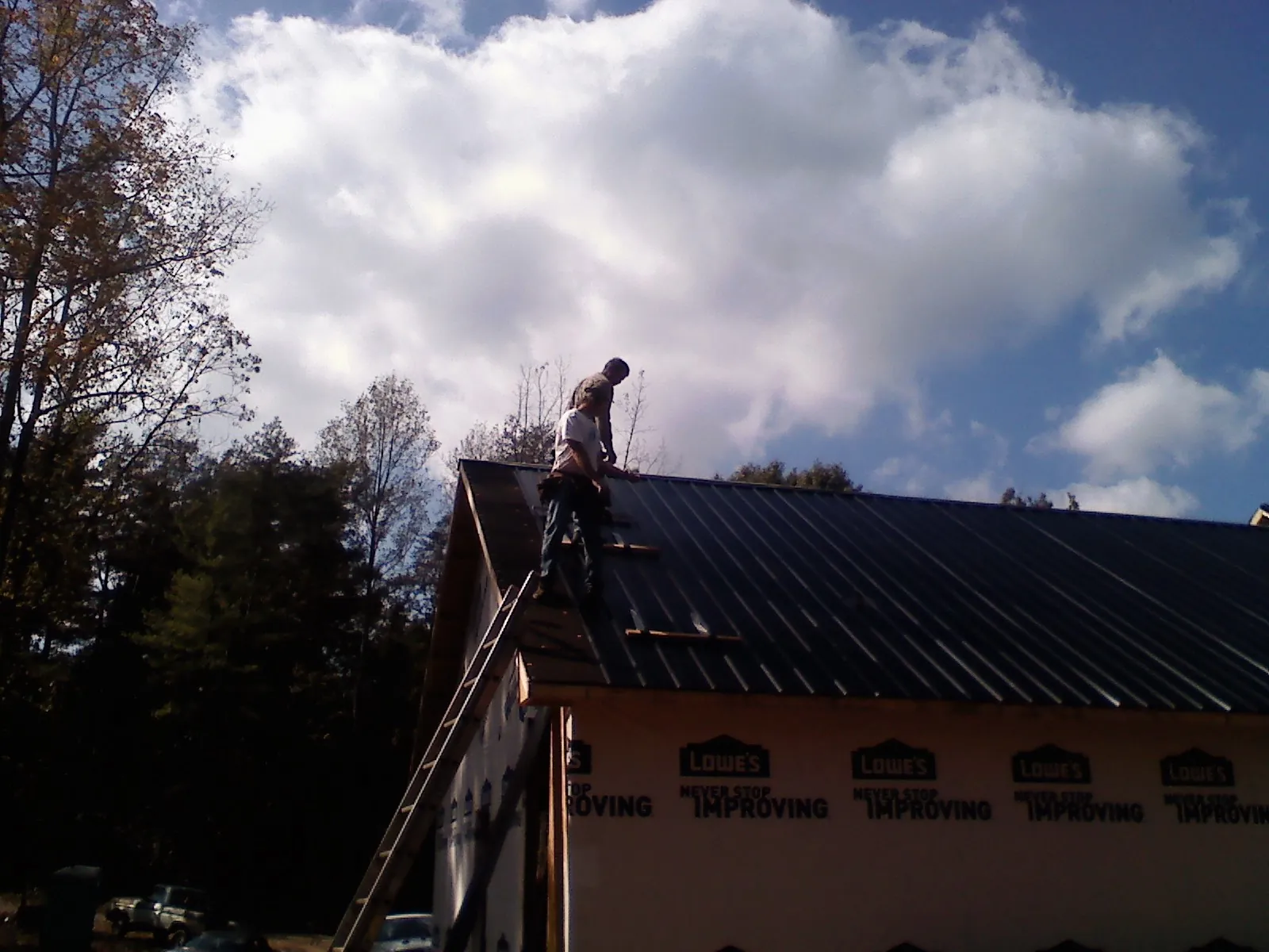 Roofer fastening dark metal panels high against a cloudy sky, from a Roof Inspection job in Dammeron Valley
