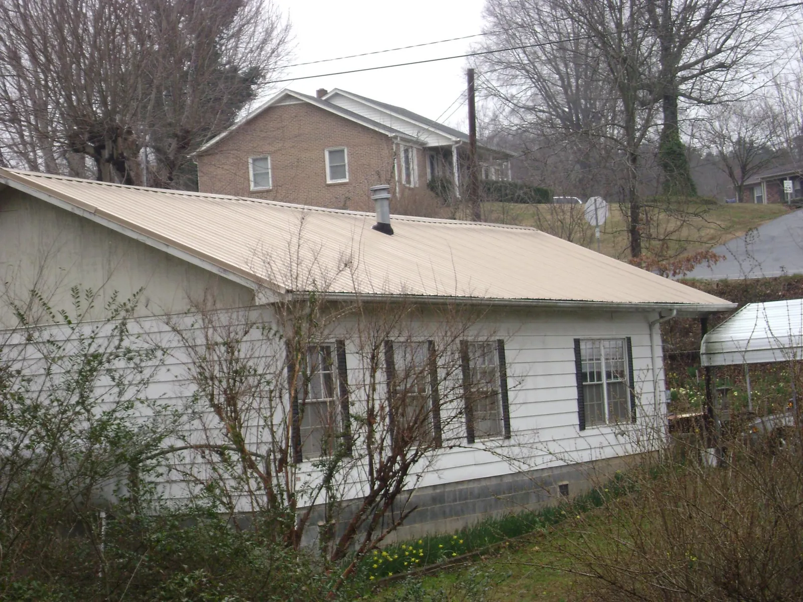 Tan metal roof on a white sided house set into a hillside — Commercial Roofing by Roofing Brothers in Dammeron Valley